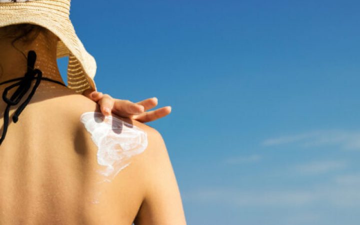 Woman in a hat applying sunscreen on her shoulder